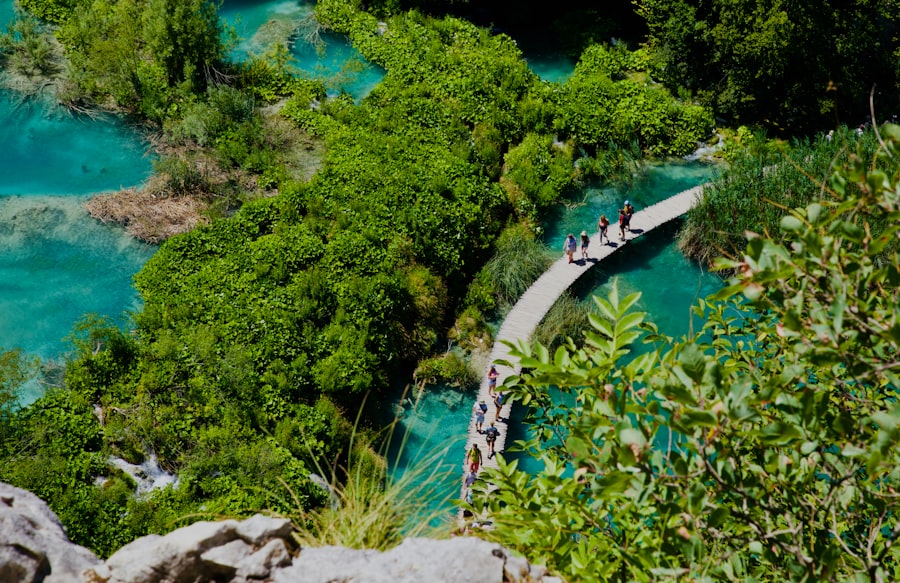 a group of people walking on a path by a body of water with Plitvice Lakes National Park in the background