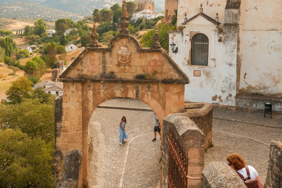 People walk through an ancient stone archway with buildings beyond