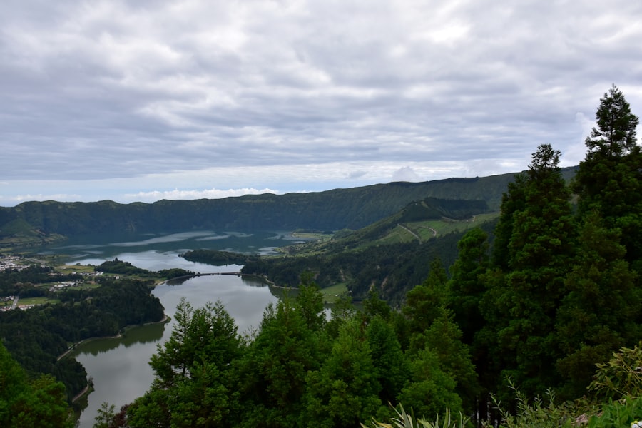Lush green hills surround tranquil lakes under cloudy sky.