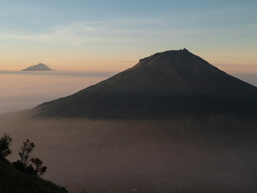 A large volcanic mountain peak rising above a thick layer of low clouds