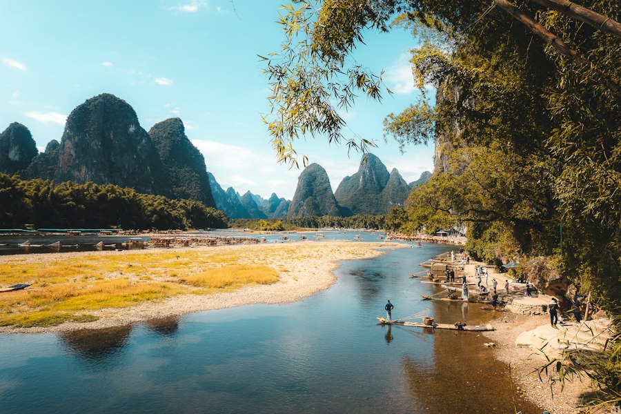Karst mountains rise above a tranquil river with bamboo trees