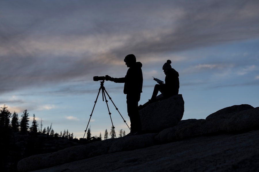 a man standing on a rock with a camera and a man sitting on a tripod