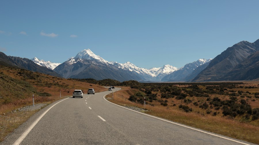 Cars driving on a winding road towards snow-capped mountains