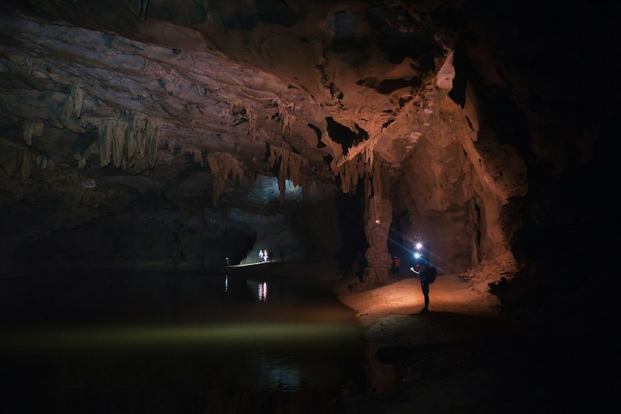 People with headlamps exploring a dark cavern with a subterranean pool and stalactites