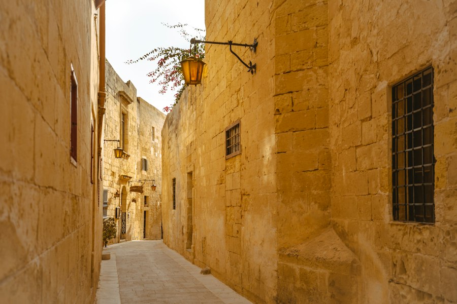 A narrow stone alleyway with hanging lanterns and blooming bougainvillea in Mdina, Malta