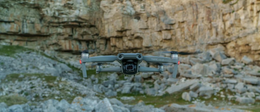 A drone flies in front of a rocky cliff face
